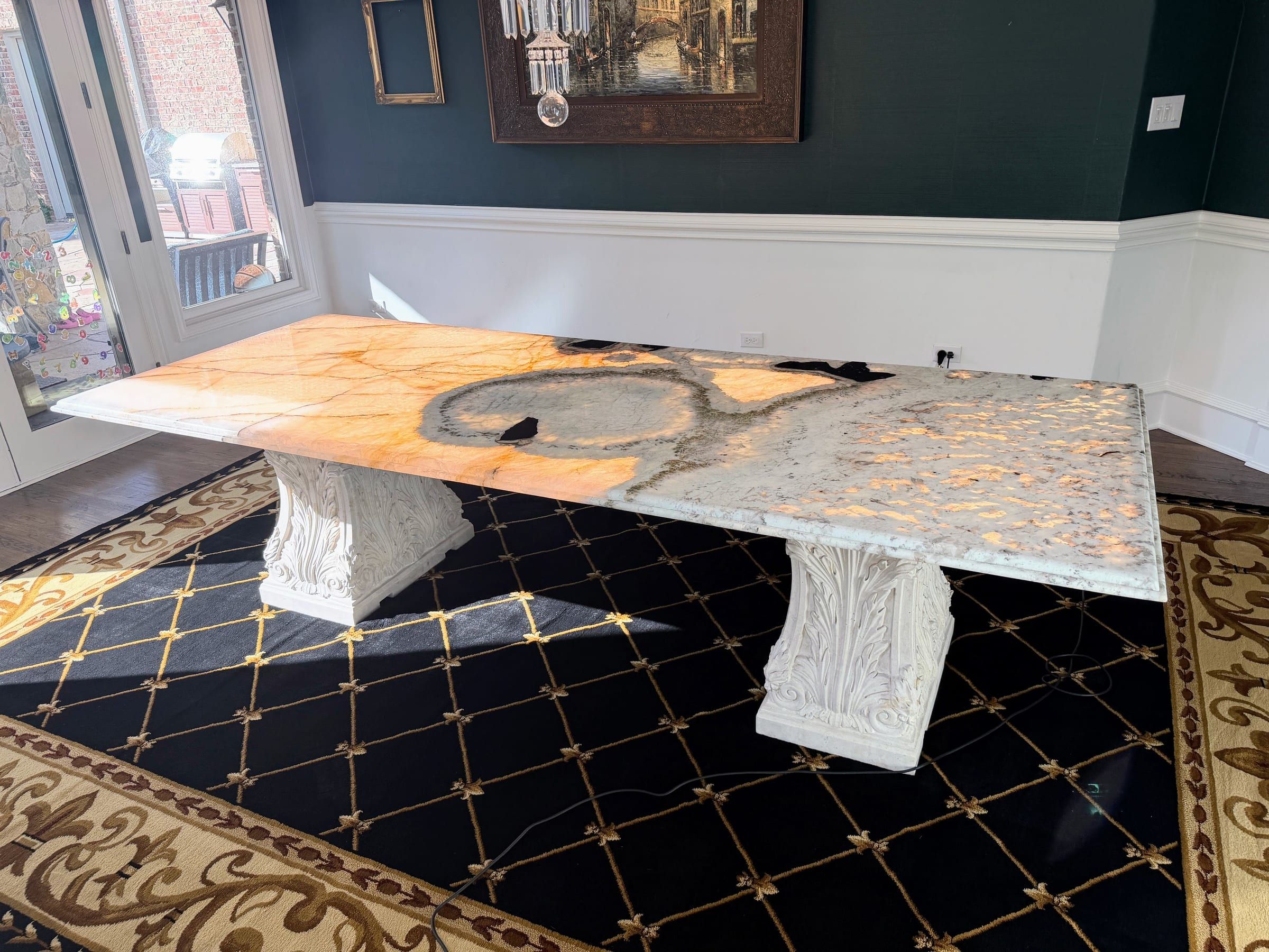 A large custom backlit mixed stone dining table featuring ornate white pedestals and glowing amber and white patterns.