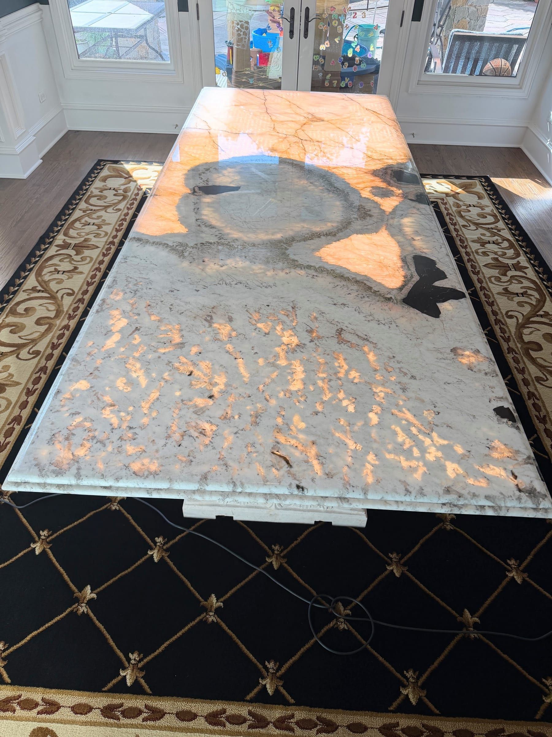 A large custom backlit natural stone dining table featuring glowing amber and white translucent veining.