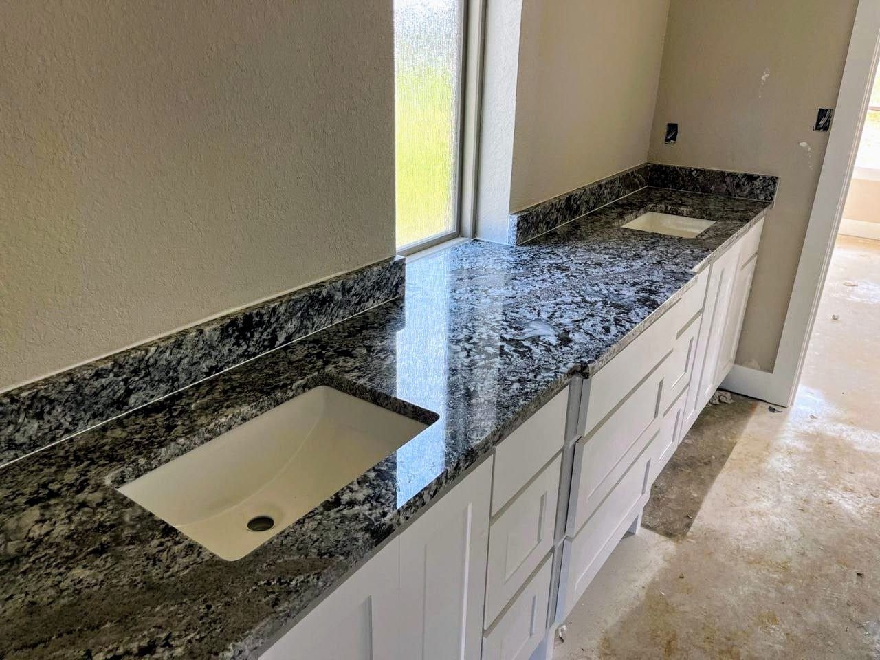 A double bathroom vanity featuring black and white granite countertops with integrated white sinks in a newly constructed room.