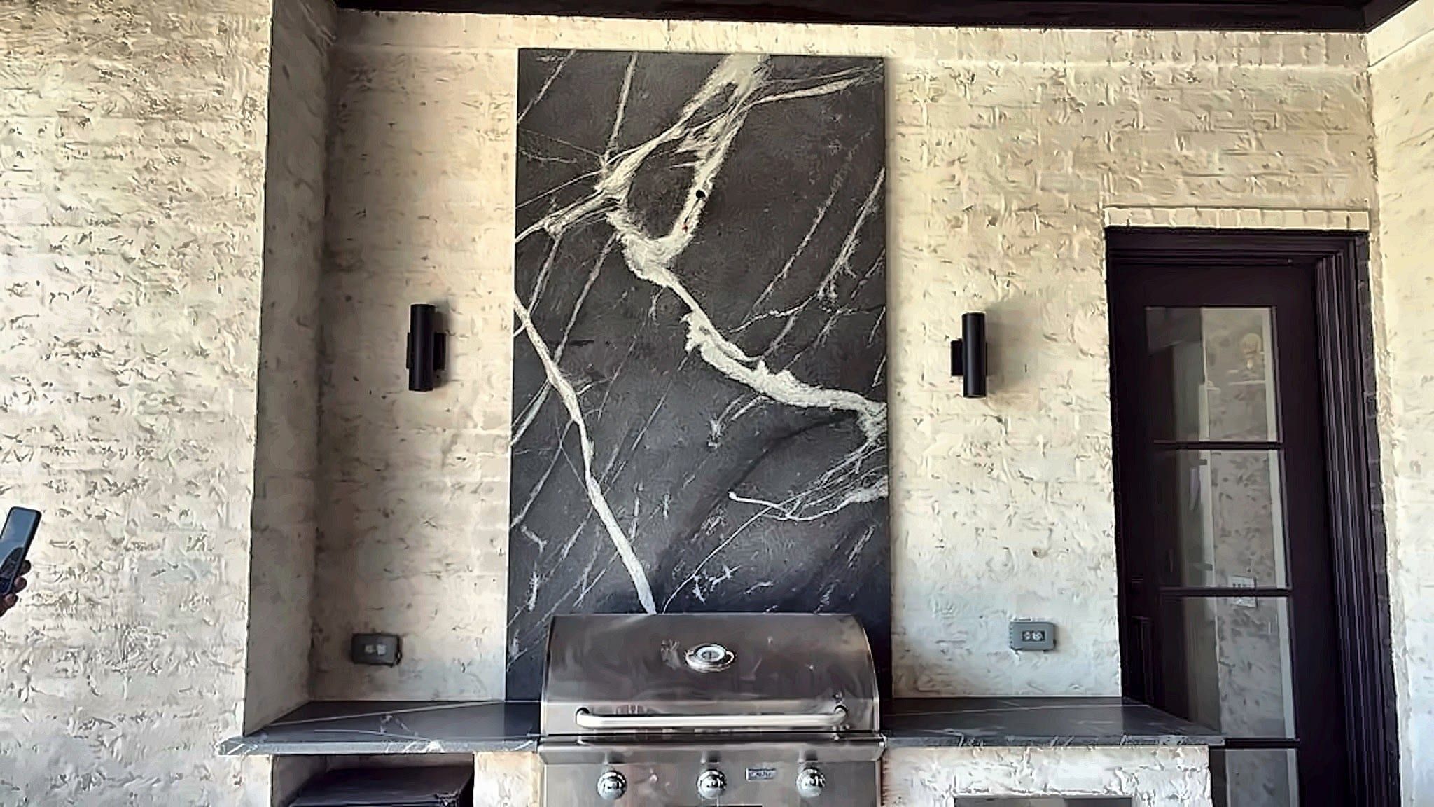 Black marble slab with prominent white veining serves as a dramatic backsplash above an outdoor kitchen grill.