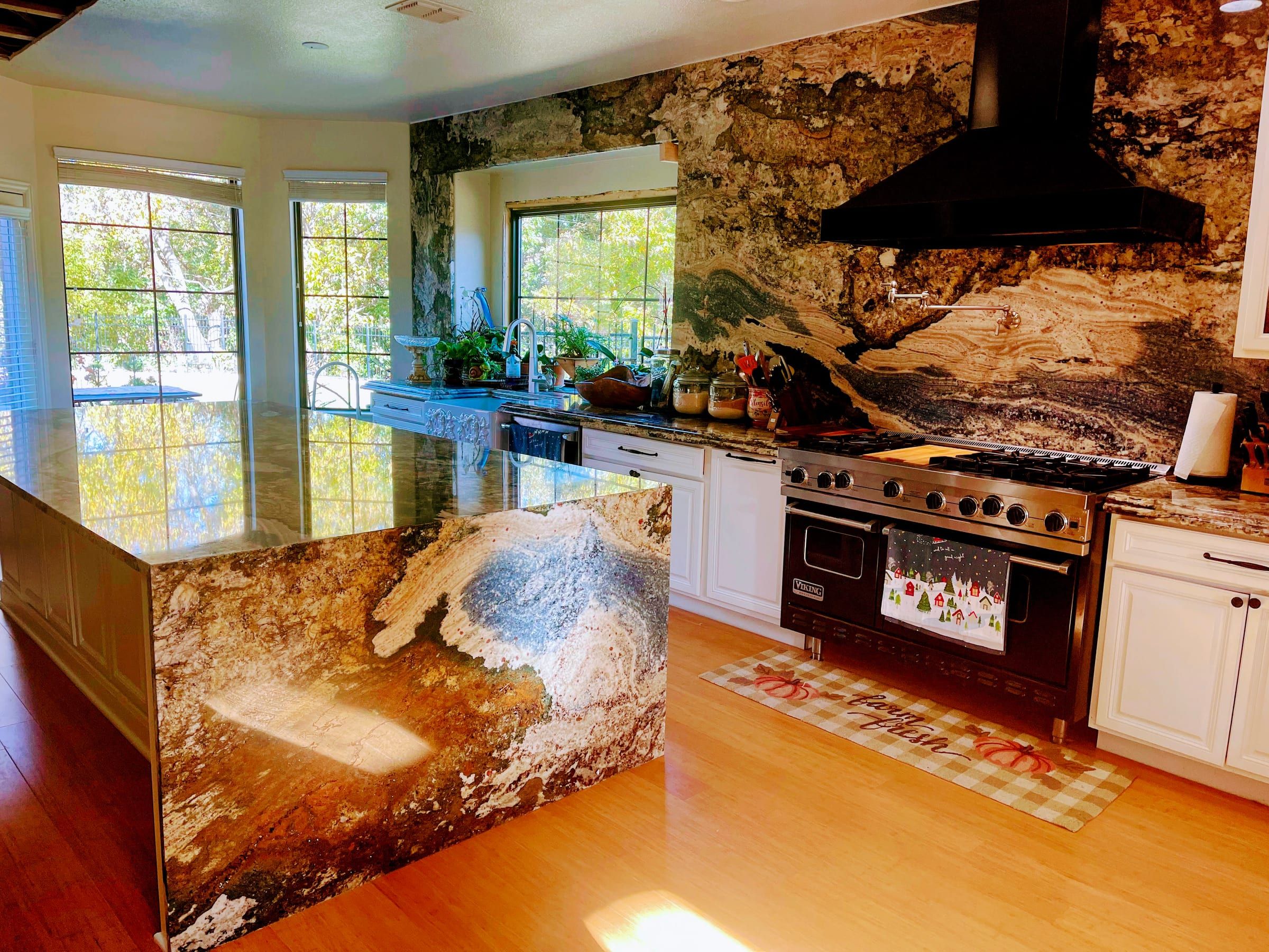 A kitchen featuring a dramatic granite waterfall island and a matching full-height granite backsplash with bold, earthy veining.