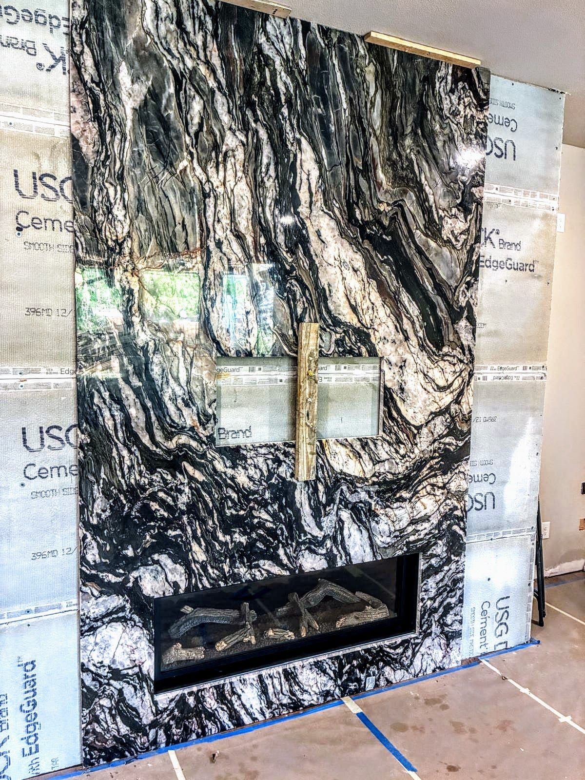A floor-to-ceiling fireplace surround clad in dramatic black, white, and grey book-matched marble with a linear gas firebox.