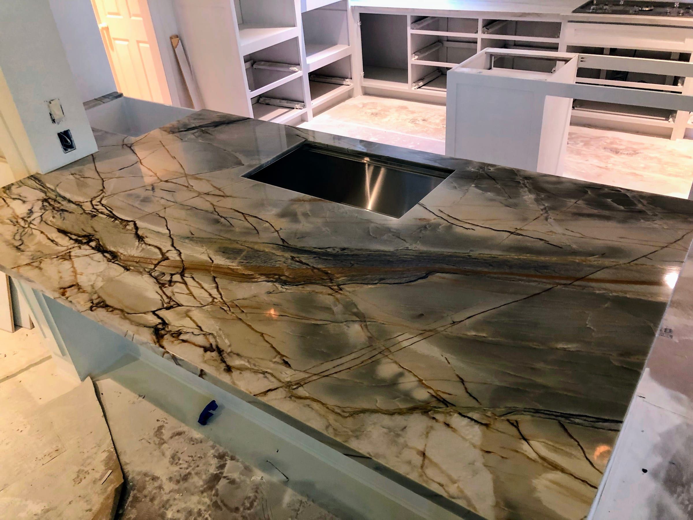A kitchen island featuring a dramatic, heavily veined quartzite countertop with deep brown and grey tones and an undermount sink.