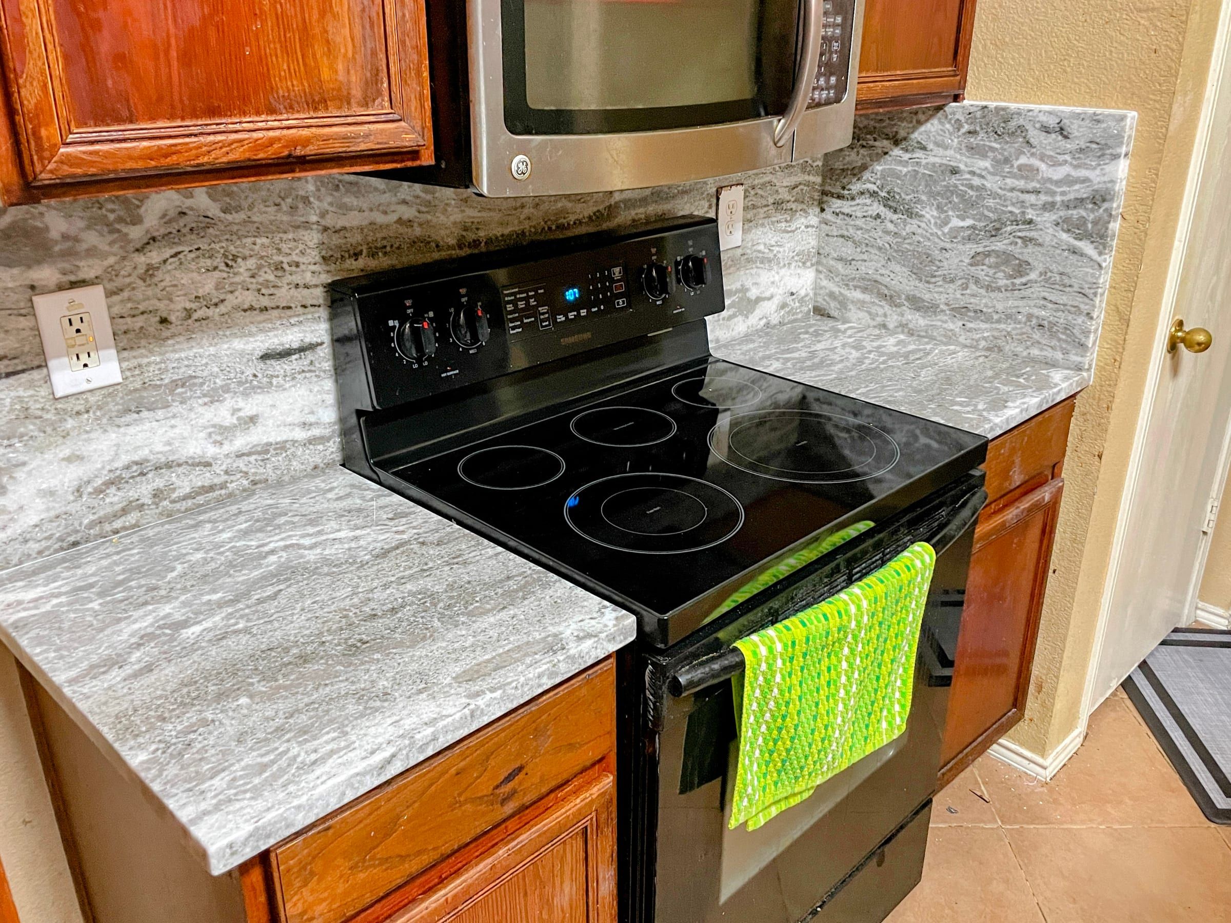 Grey and white veined marble countertops and backsplash wrapping a black range, framed by warm wood cabinetry.