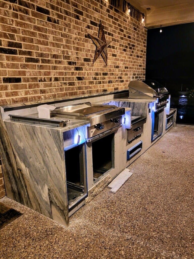 An outdoor kitchen featuring grey and white marble countertops with dramatic veining and integrated stainless steel appliances.