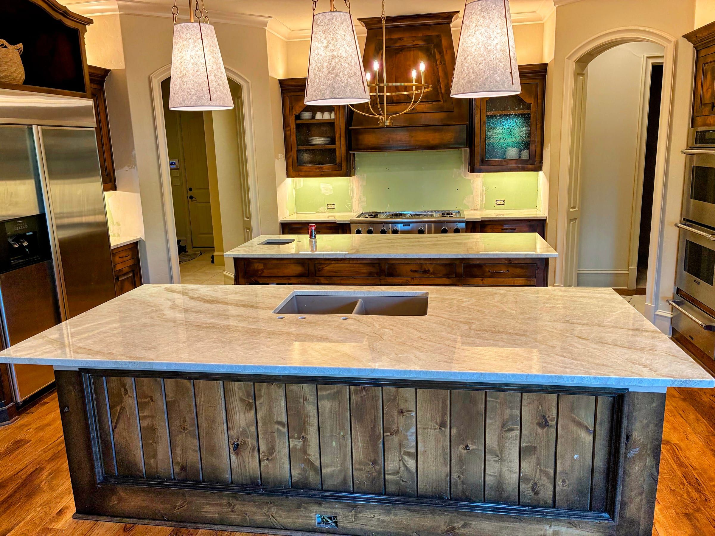 A spacious kitchen with a light grey and white marble island countertop with soft veining, set on a wood-plank island base with dark stained perimeter cabinets.