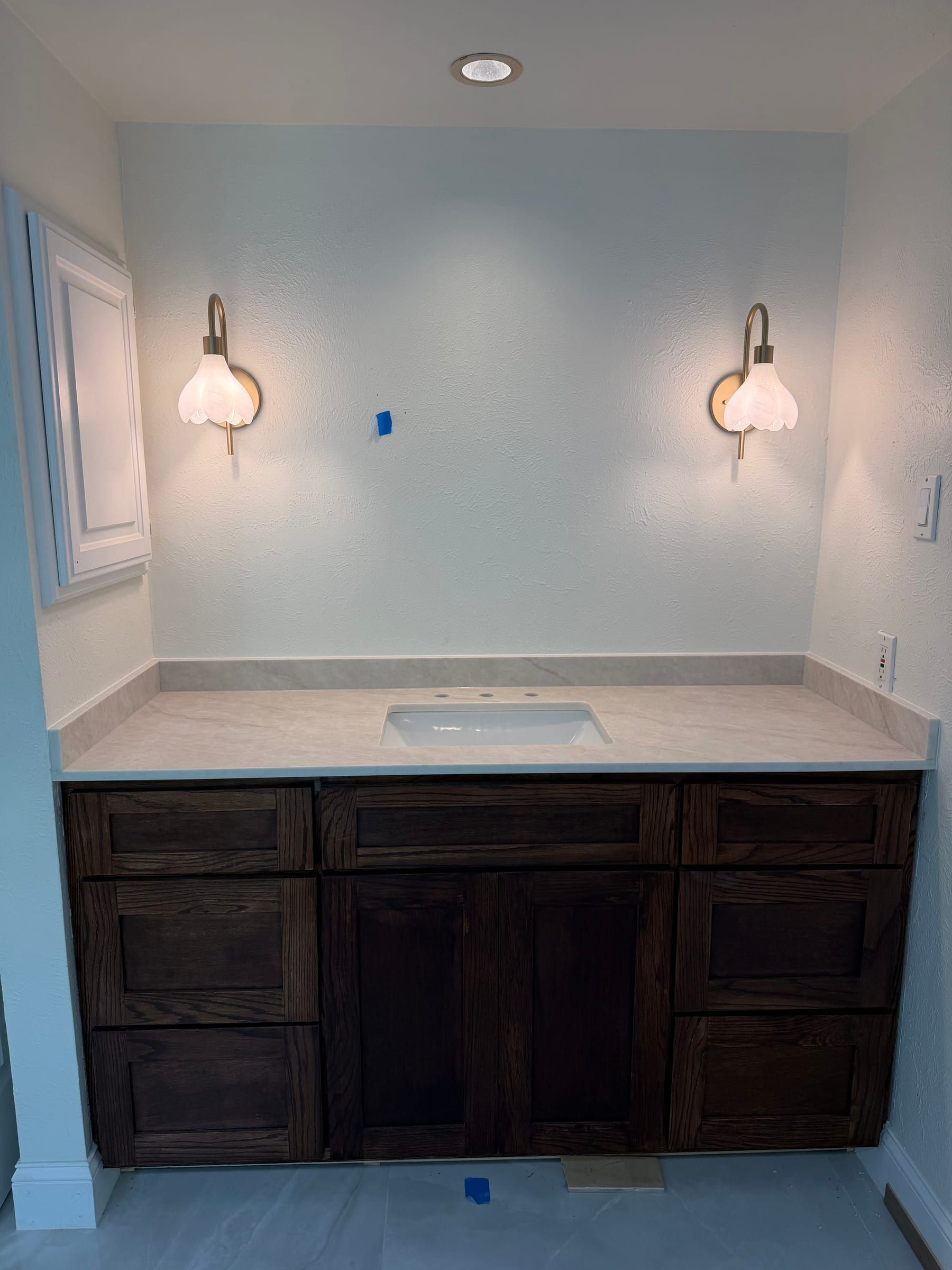 Light marble bathroom vanity with dark wood cabinets and a built-in sink beneath dual gold wall sconces.
