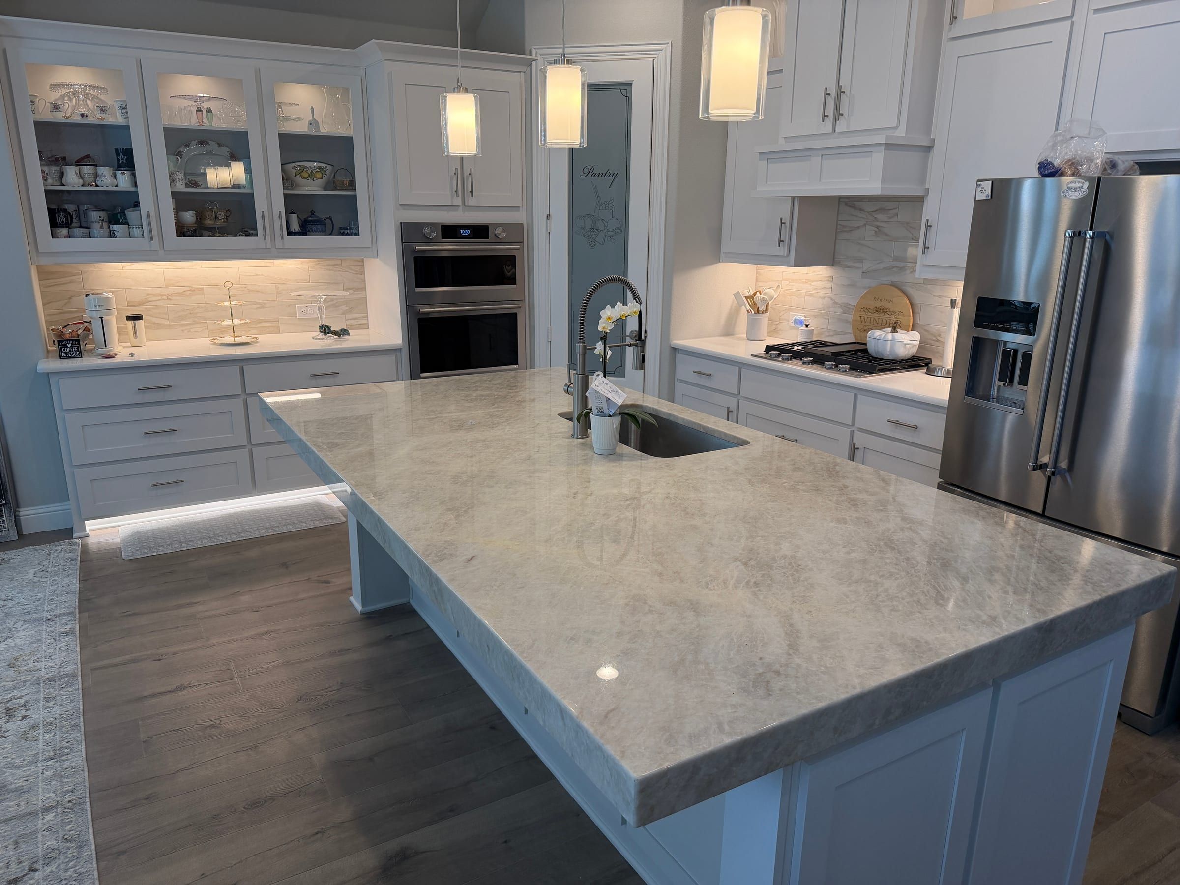 A large kitchen island featuring a light-toned, natural stone countertop with subtle veining and a thick mitered edge in a bright white kitchen.