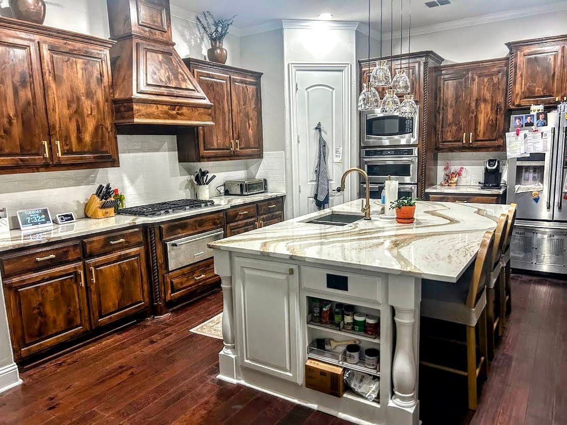 A kitchen island featuring a white quartz countertop with bold, flowing brown and gold veining, paired with dark wood cabinets and a white base.