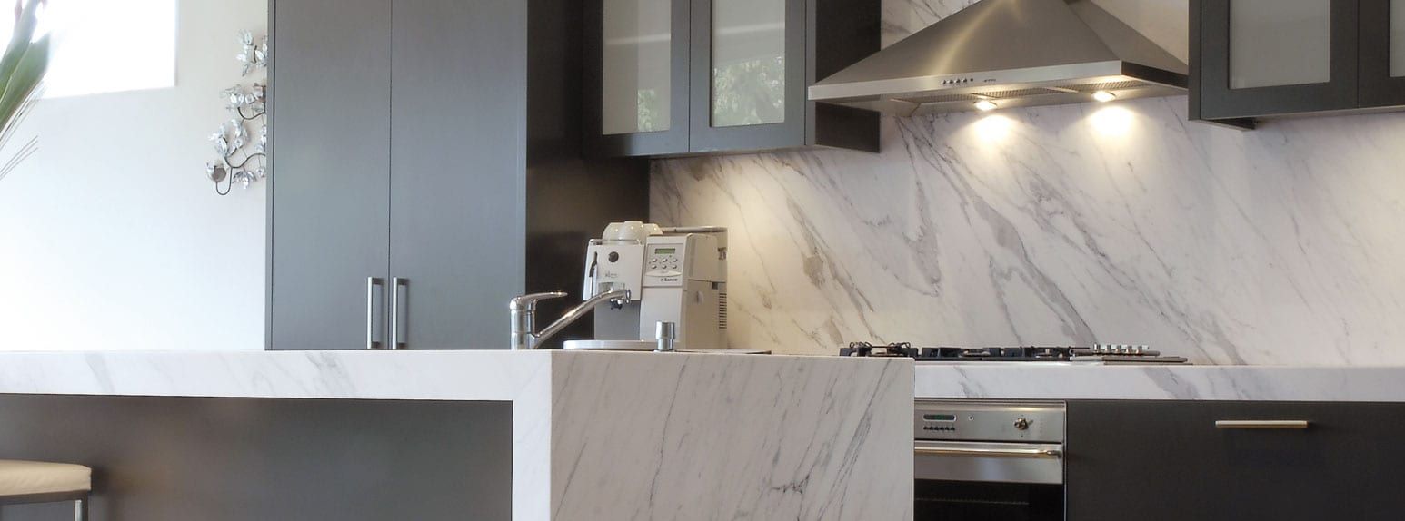 Kitchen with dark cabinetry and a white and grey marble-look Tajams quartz island and backsplash with soft veining.