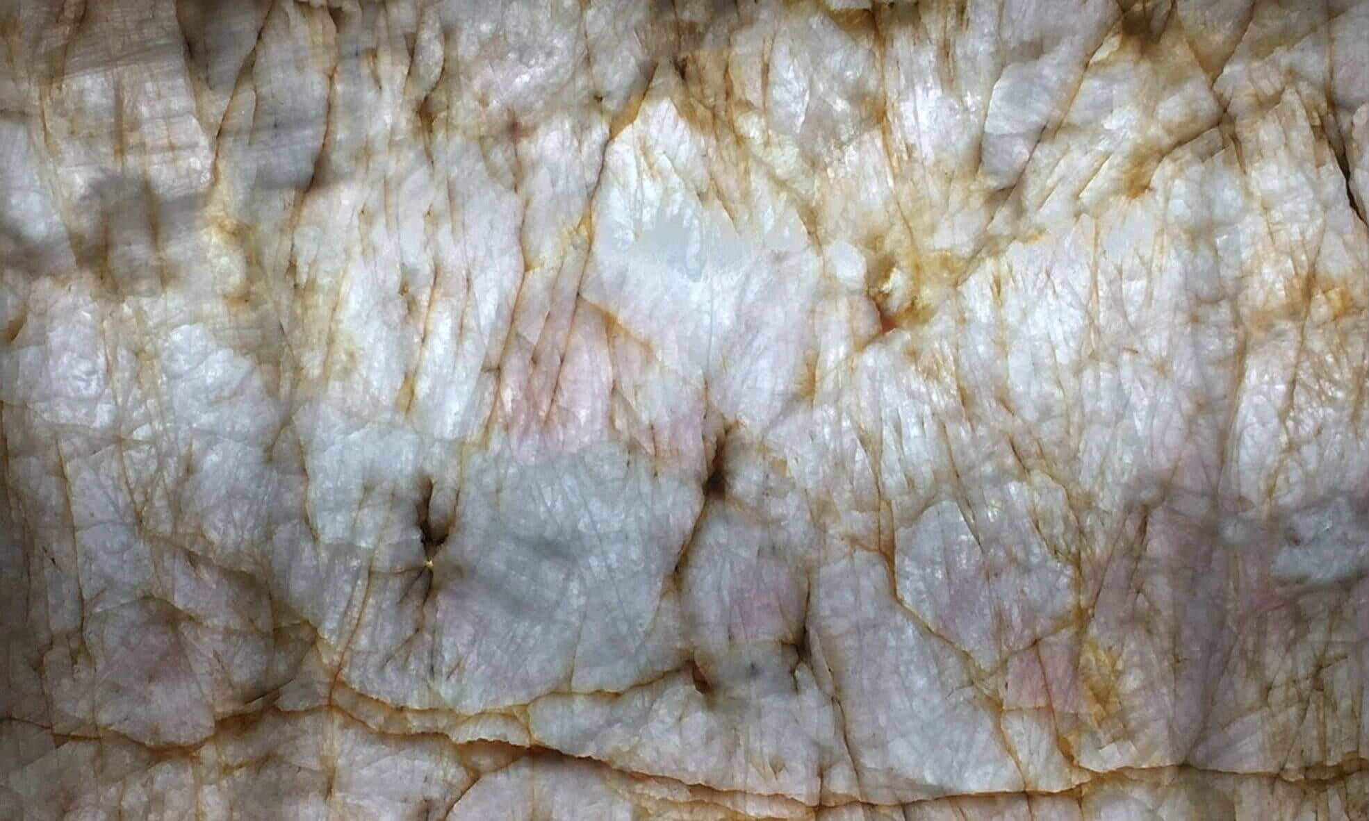 Close-up of a translucent, backlit quartzite slab from Verona Marble with warm amber and rust veining through white crystalline stone.