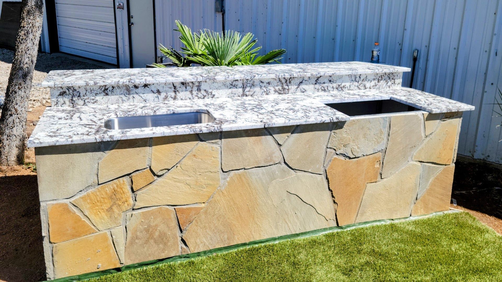 An outdoor kitchen island featuring a white granite countertop with black veining and a rustic flagstone base.