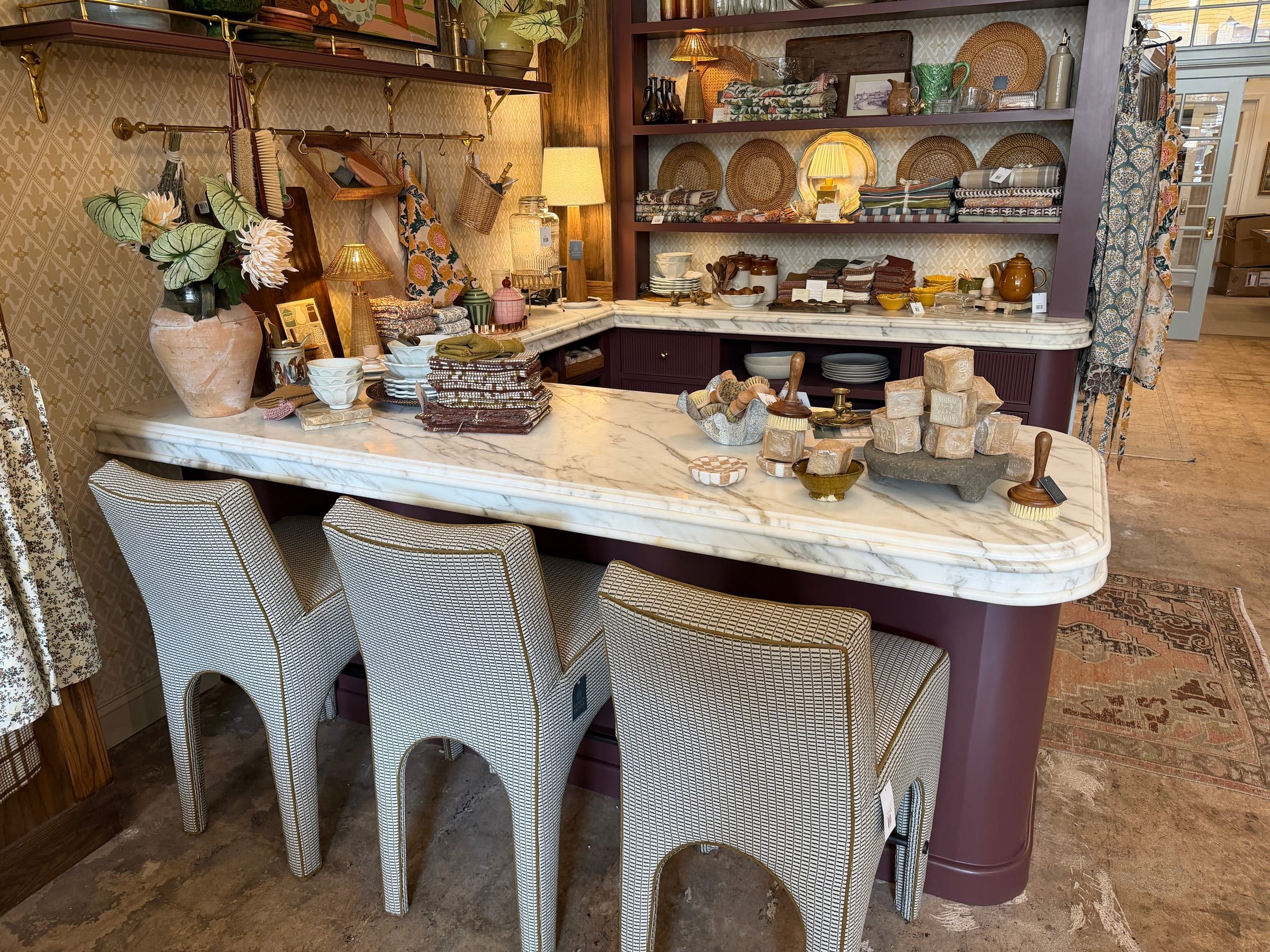 A white marble countertop with soft gray veining used as a display surface in a retail store with upholstered bar stools.