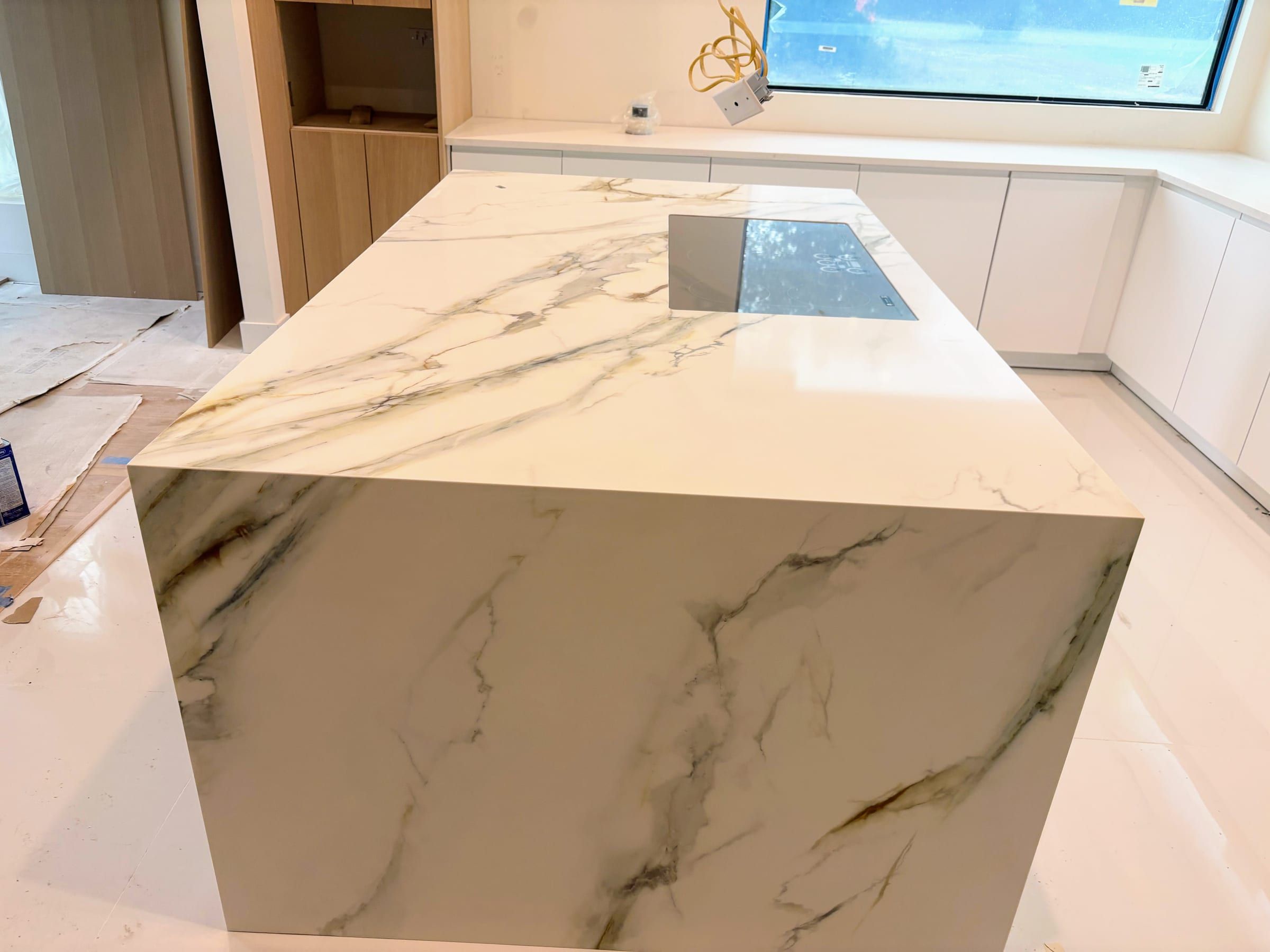 A large waterfall kitchen island featuring white marble with dramatic grey and gold veining and an integrated cooktop.
