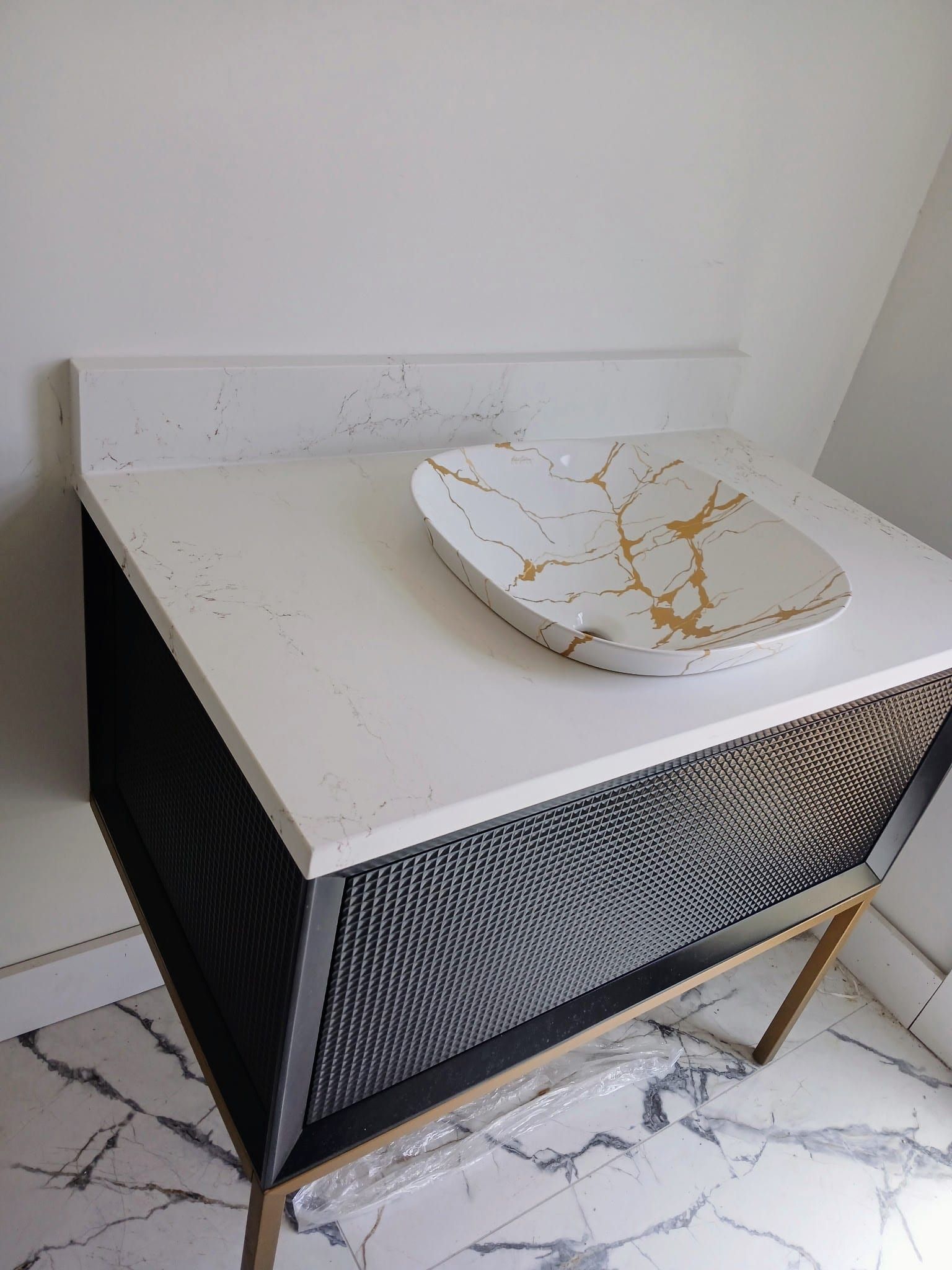 A white quartz bathroom vanity countertop with subtle grey veining featuring a vessel sink with gold veining details.