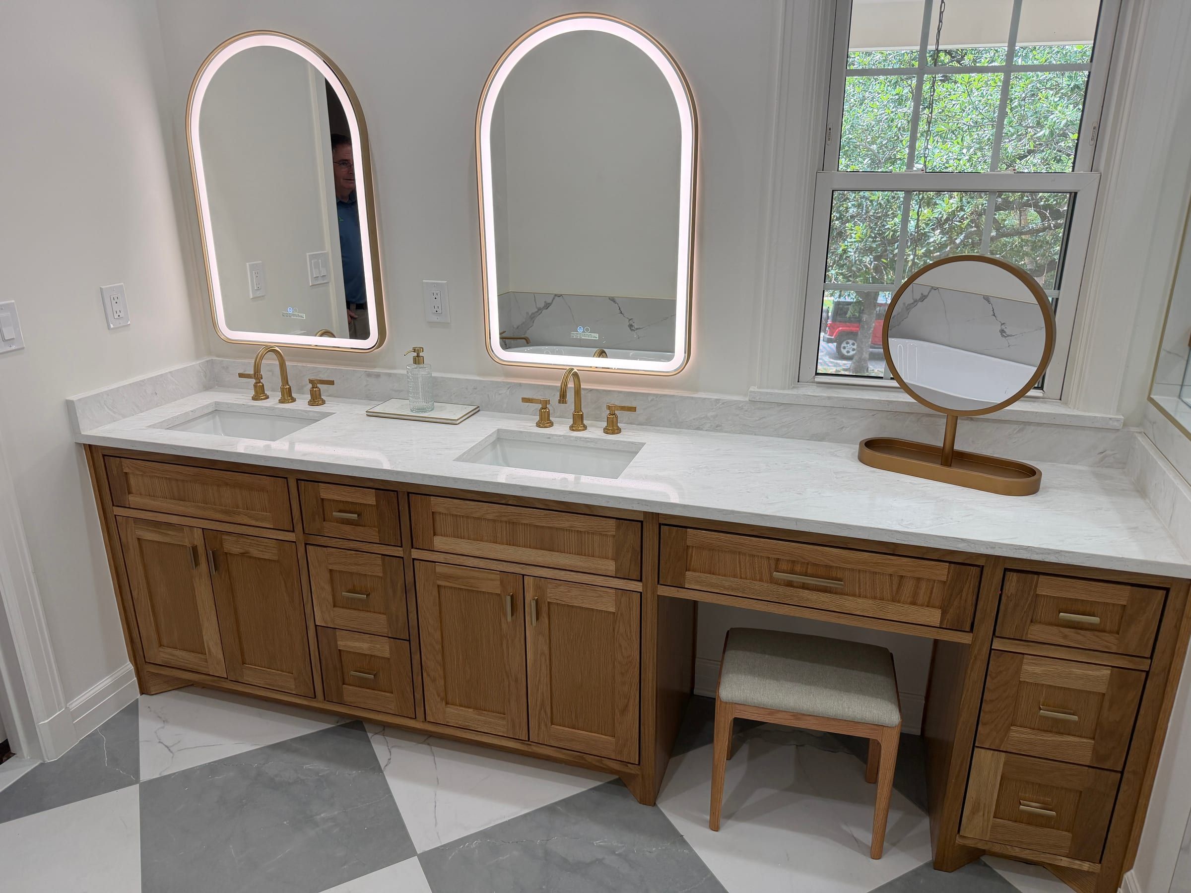 A double bathroom vanity featuring a white quartz countertop with subtle grey veining, paired with natural wood cabinetry and gold fixtures.