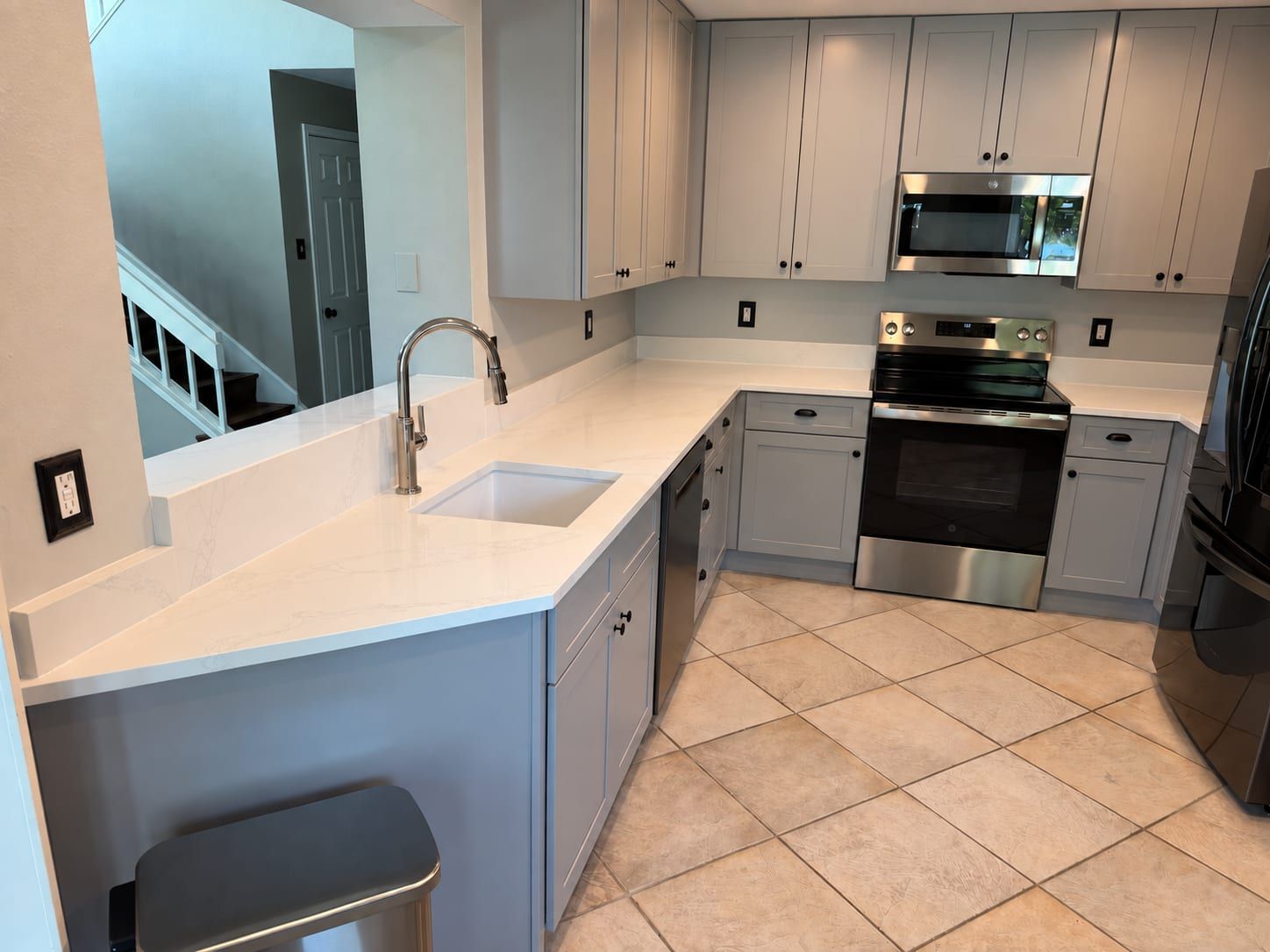 L-shaped white quartz countertop with subtle grey veining featuring an under-mount sink, curved pass-through wall, and matching backsplash in a modern kitchen.
