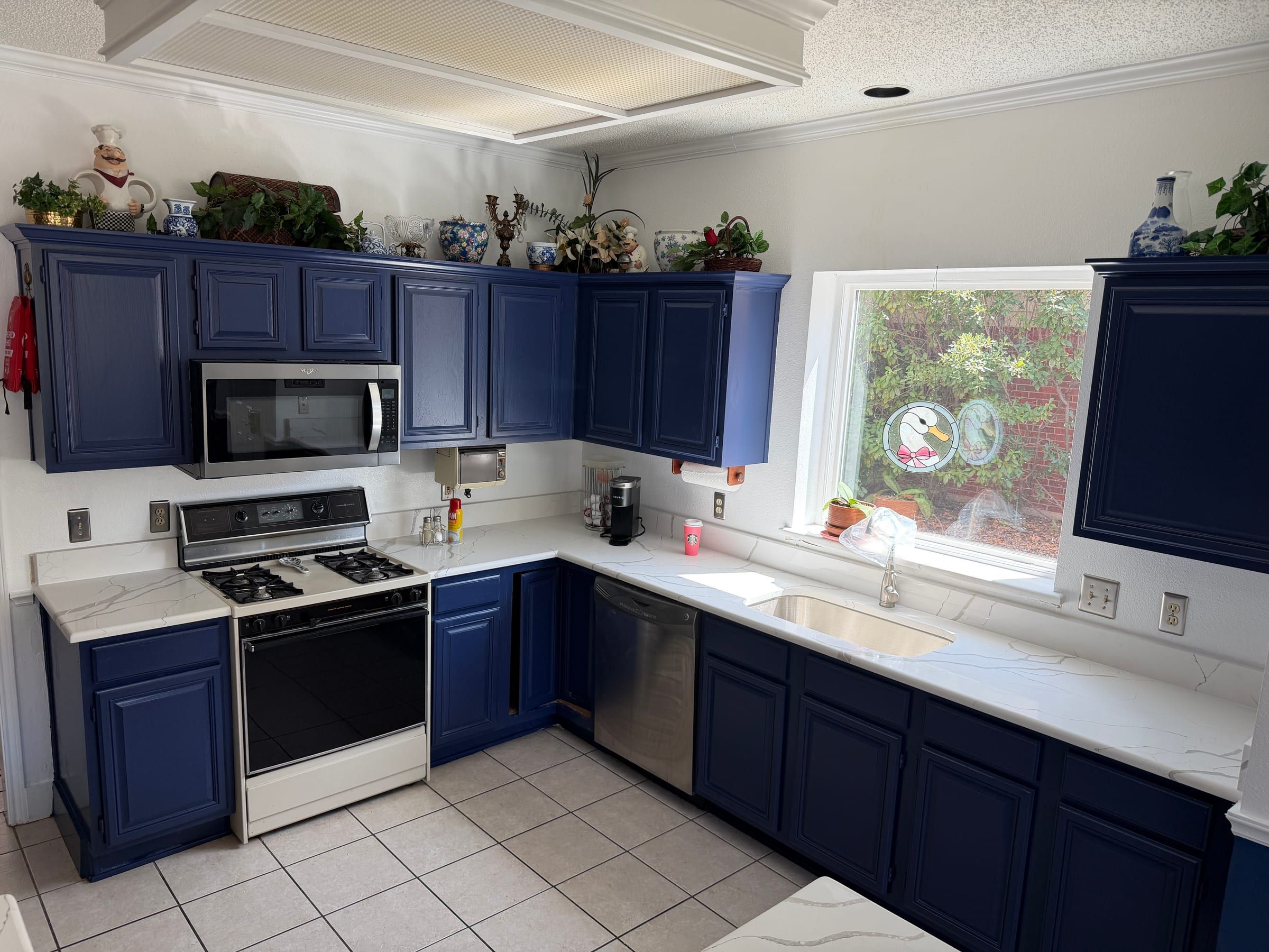 White quartz countertops with delicate gray veining pair with bold blue cabinets and stainless steel appliances in a bright kitchen.