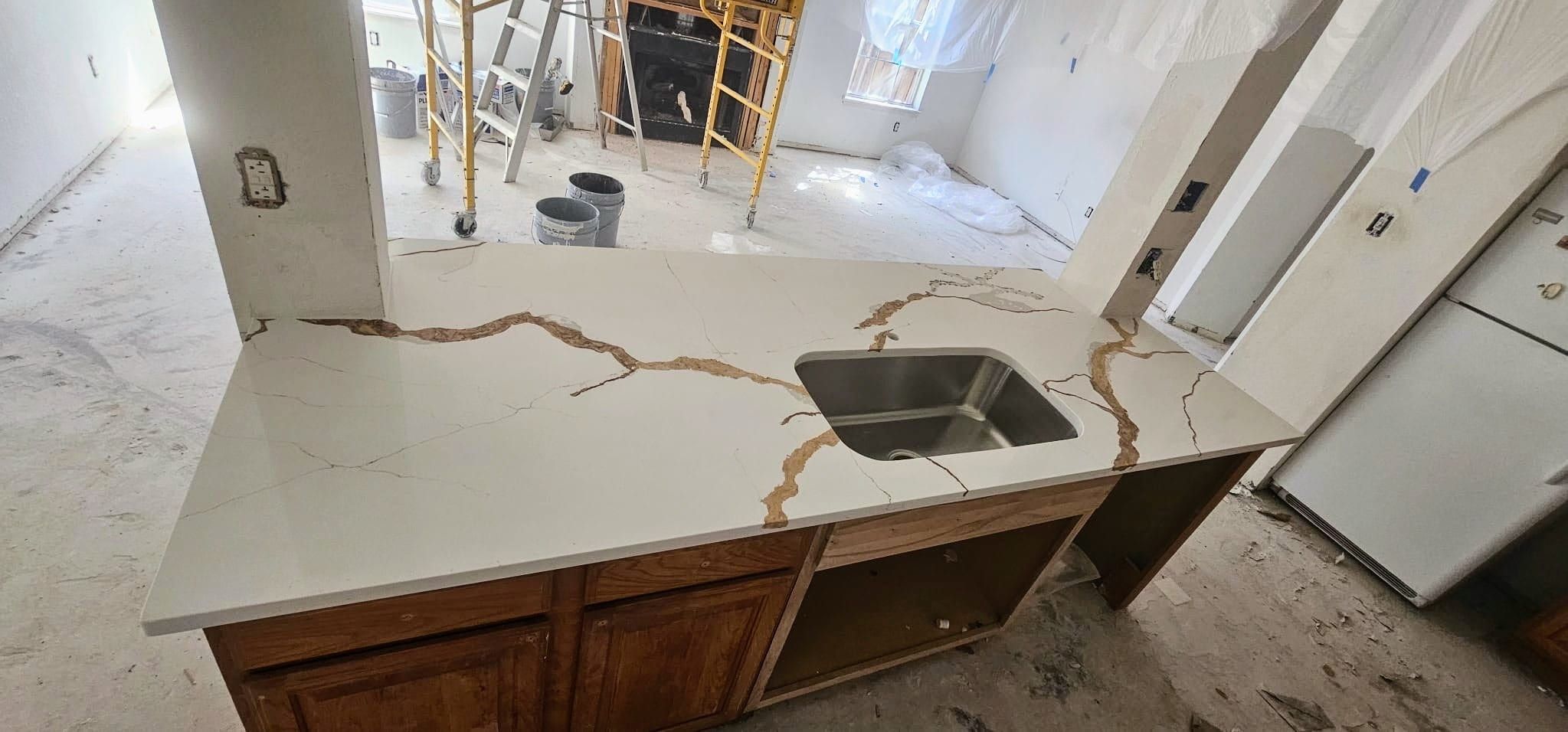 White quartz kitchen island countertop featuring dramatic bold gold veining and an undermount stainless steel sink during home renovation.