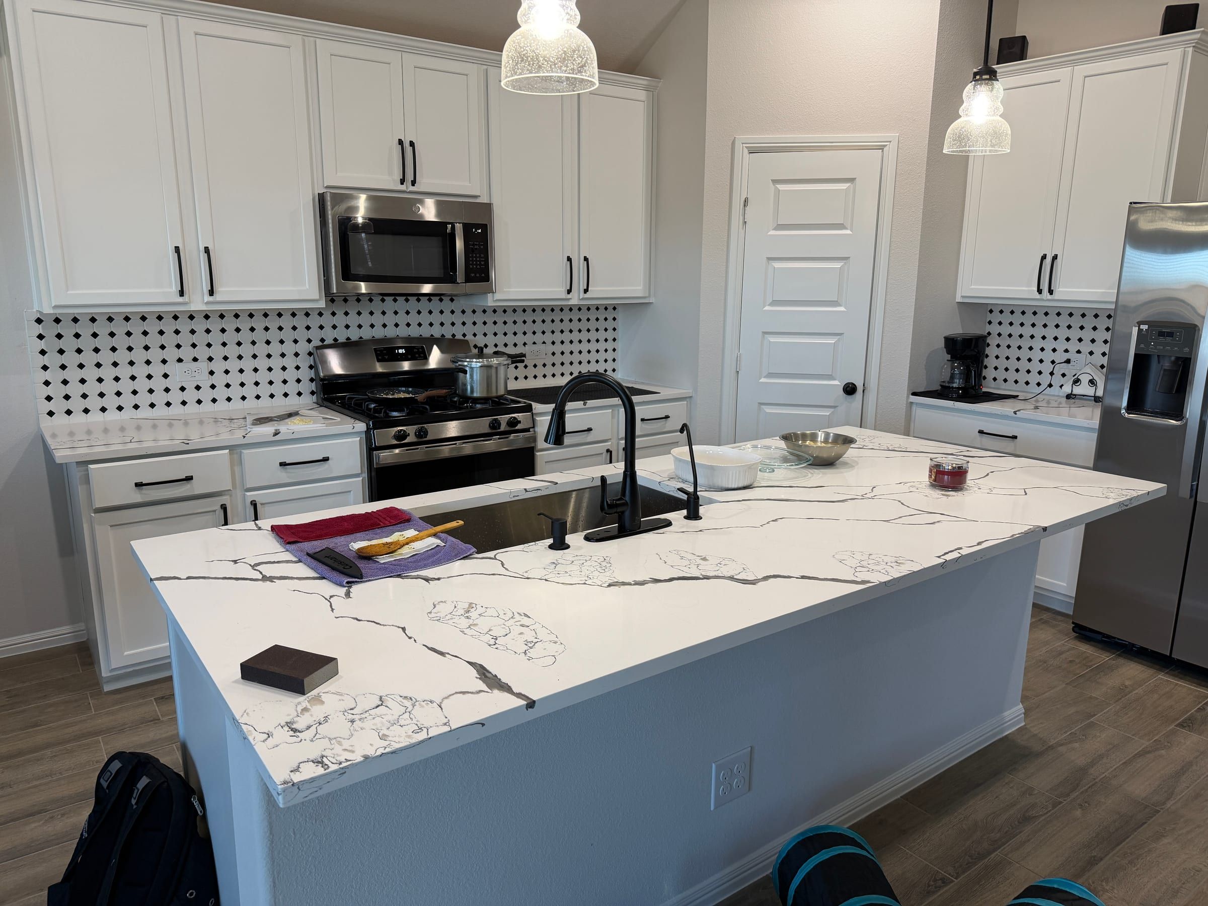 A kitchen island featuring white quartz countertops with bold black veining and a black faucet, set against white cabinets and a patterned backsplash.
