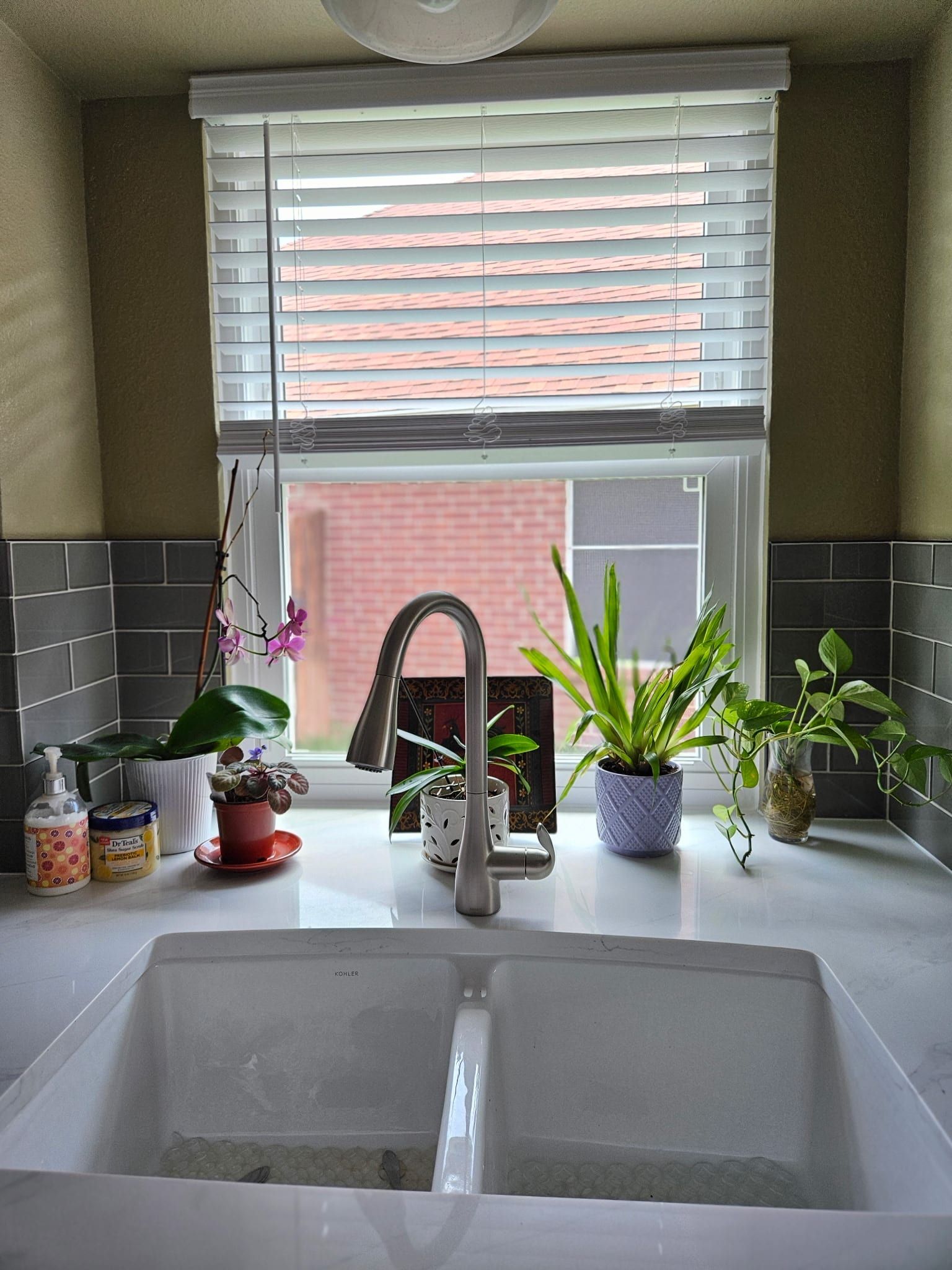 White quartz countertop with subtle grey veining surrounding a white farmhouse sink in a kitchen with grey subway tile backsplash.