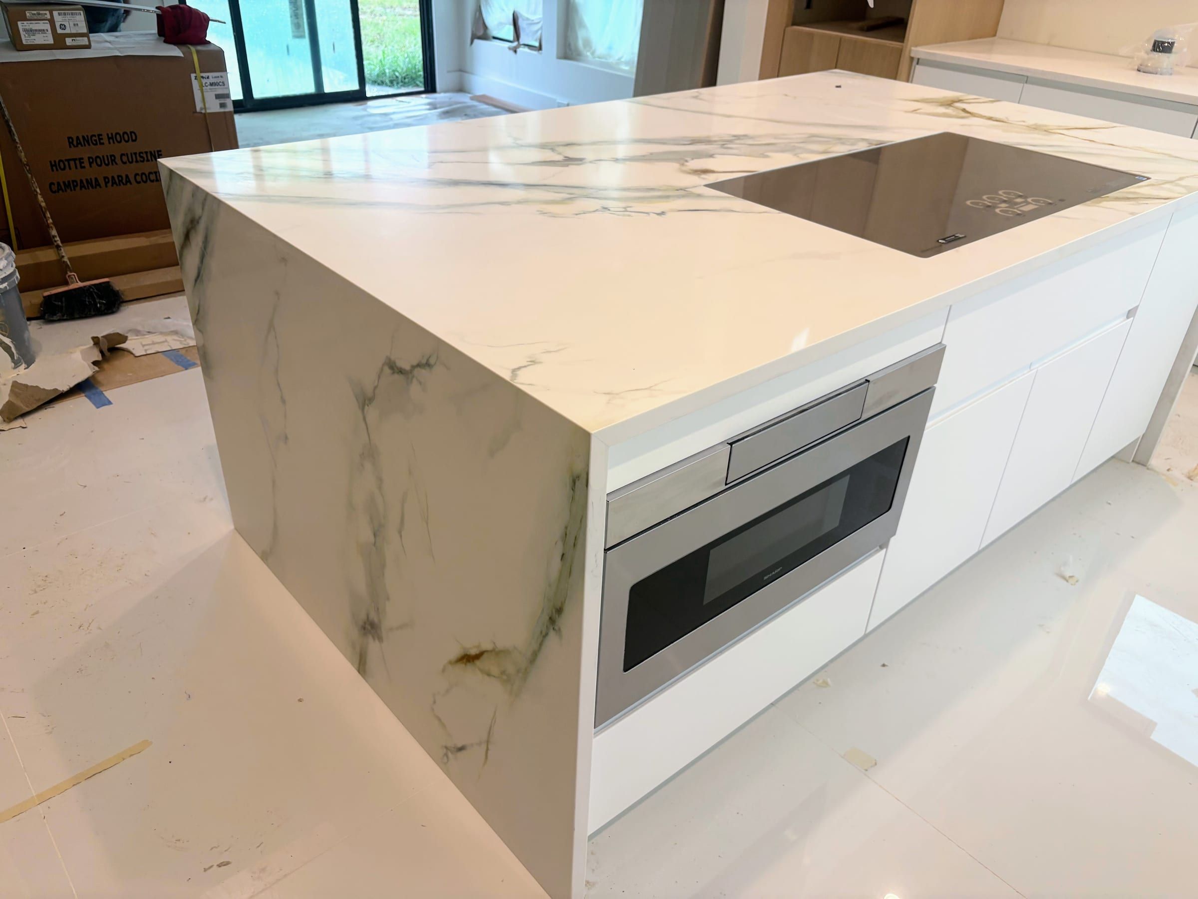 A large kitchen island featuring white engineered quartz with striking grey and green veining and a waterfall edge.