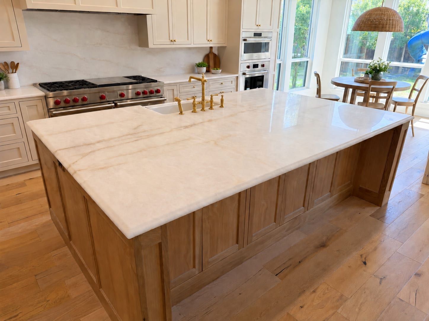 Large kitchen island featuring a white quartzite countertop with subtle warm veining and a brass faucet set against a natural wood base.